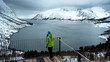 Lofoten islands, Senja region, Norway. Winter. Young girl in green jacket and blue hat stands on observation deck, looking at Bay of ocean. In background snowy mountains. Concept of tourism.