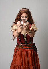 close up portrait of beautiful red haired woman wearing a medieval maiden, fortune teller costume. Posing while  holding a  crystal ball. isolated on studio background.