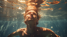 man swimming underwater with sunlight shining on face through ripples