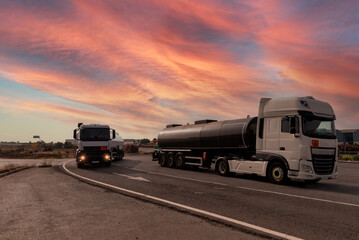 Wall Mural - Two tankers with dangerous goods, one parked and one driving under a dramatic sky at dawn.