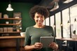 © Georgii - Half-length portrait of cheerful African American businesswoman in business attire holding a tablet. Happy smiling young lady, successful entrepreneur or employee working in office or coworking cafe.