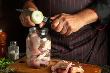 Wall Mural - Cooking salted fish in a jar with onions and spices according to an old recipe. Chef's hands cutting an onion with a knife