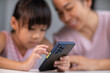 © scentrio - Happy Asian family mother and cute daughter using phone together at home. Mother and little girl laughing happily using smartphone watching funny social media video app sitting at table together.