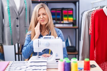 Poster - Blonde woman dressmaker designer using sew machine touching mouth with hand with painful expression because of toothache or dental illness on teeth. dentist concept.