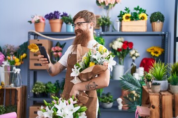 Wall Mural - Young redhead man florist using smartphone holding flowers at flower shop