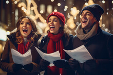 Three Cheerful Friends Doing Door-to-door Carol Singing On Christmas Eve. Group Of Young People Caroling On The Street During Festive Holidays. Traditional Christmas Activities.