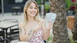 © Krakenimages.com - Young blonde woman pointing to dollars sitting on table at coffee shop terrace