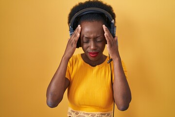 Wall Mural - African woman with curly hair standing over yellow background wearing headphones with hand on head for pain in head because stress. suffering migraine.