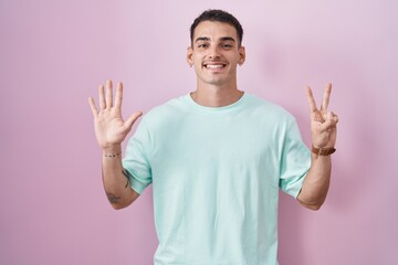 Canvas Print - Handsome hispanic man standing over pink background showing and pointing up with fingers number seven while smiling confident and happy.