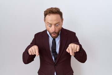 Sticker - Middle age business man with beard wearing suit and tie pointing down with fingers showing advertisement, surprised face and open mouth