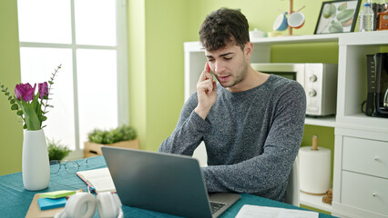 Sticker - Young hispanic man talking on smartphone using laptop at dinning room