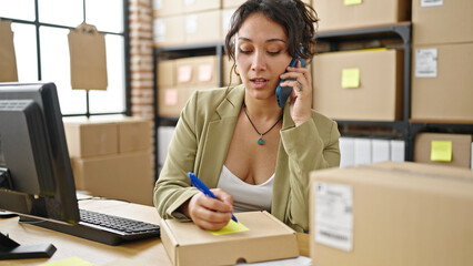 Canvas Print - Young beautiful hispanic woman ecommerce business worker talking on smartphone writing on package at office