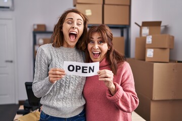 Poster - Two women working at small business ecommerce holding open banner smiling and laughing hard out loud because funny crazy joke.