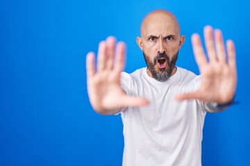 Poster - Hispanic man with tattoos standing over blue background doing stop gesture with hands palms, angry and frustration expression