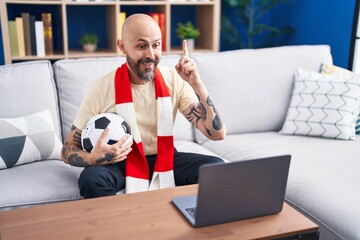 Wall Mural - Hispanic man with tattoos watching football match hooligan holding ball on the laptop surprised with an idea or question pointing finger with happy face, number one