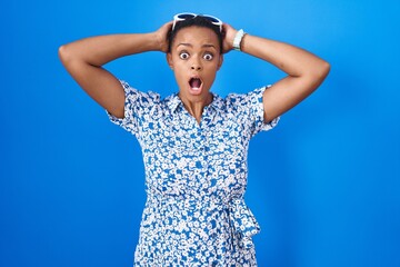 Poster - African american woman standing over blue background crazy and scared with hands on head, afraid and surprised of shock with open mouth