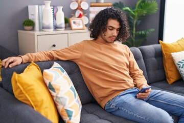 Poster - Young latin man using smartphone sitting on sofa at home