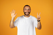 Cheerful Man Holding Up Five Fingers And Peace Sign On Orange Backdrop