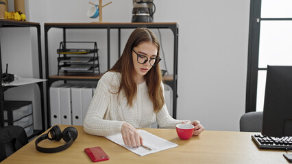 Poster - Young hispanic woman business worker writing on documents holding cup of coffee at office