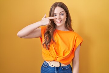 Sticker - Caucasian woman standing over yellow background pointing with hand finger to face and nose, smiling cheerful. beauty concept