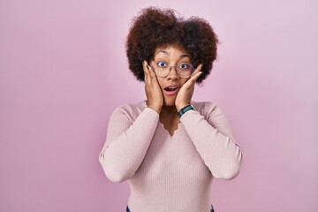 Canvas Print - Young african american woman standing over pink background afraid and shocked, surprise and amazed expression with hands on face