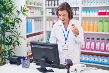 Poster - Middle age woman pharmacist using computer holding pills bottle at pharmacy