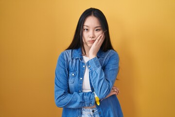 Canvas Print - Young asian woman standing over yellow background thinking looking tired and bored with depression problems with crossed arms.