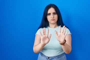 Poster - Young modern girl with blue hair standing over blue background moving away hands palms showing refusal and denial with afraid and disgusting expression. stop and forbidden.