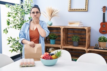 Sticker - Young girl with blue hair holding take away food at the dinning room covering mouth with hand, shocked and afraid for mistake. surprised expression