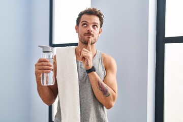 Poster - Young hispanic man wearing sportswear drinking water thinking concentrated about doubt with finger on chin and looking up wondering