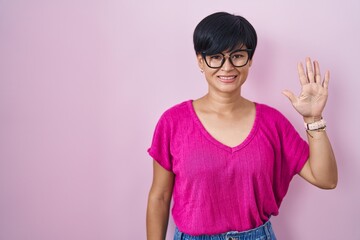 Wall Mural - Young asian woman with short hair standing over pink background showing and pointing up with fingers number five while smiling confident and happy.