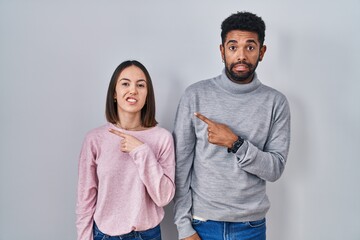 Sticker - Young hispanic couple standing together pointing aside worried and nervous with forefinger, concerned and surprised expression