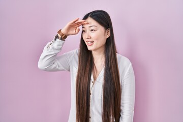 Sticker - Chinese young woman standing over pink background very happy and smiling looking far away with hand over head. searching concept.