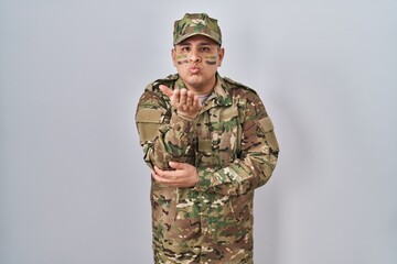 Wall Mural - Hispanic young man wearing camouflage army uniform looking at the camera blowing a kiss with hand on air being lovely and sexy. love expression.