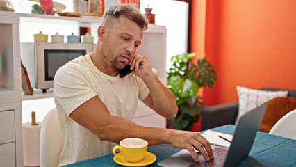 Canvas Print - Young man talking on smartphone using computer at dinning room