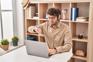 Poster - Hispanic young man wearing call center agent headset with angry face, negative sign showing dislike with thumbs down, rejection concept