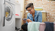 © Krakenimages.com - Young beautiful hispanic woman using smartphone waiting for washing machine at laundry room