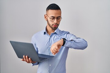 Poster - Young hispanic man working using computer laptop checking the time on wrist watch, relaxed and confident