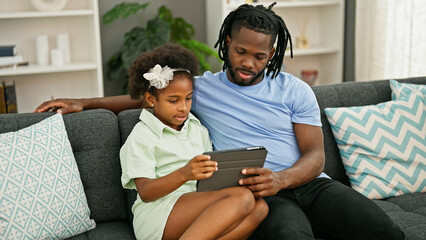 Sticker - African american father and daughter using touchpad sitting on sofa at home