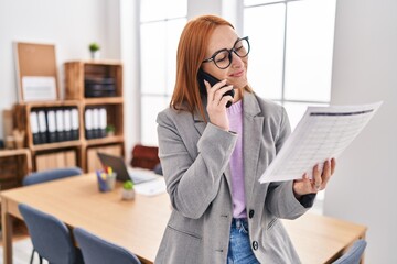 Poster - Young caucasian woman business worker talking on smartphone reading document at office