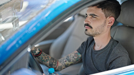 Wall Mural - Young hispanic man driving car with relaxed expression at street