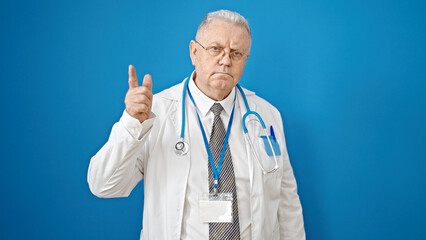 Canvas Print - Middle age grey-haired man doctor angry and stressed pointing with finger over isolated blue background