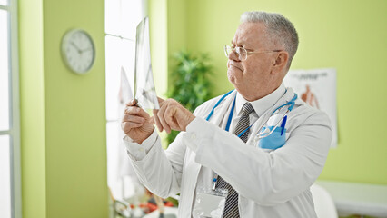 Poster - Middle age grey-haired man doctor looking xray at clinic