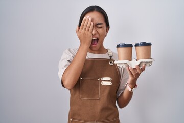 Wall Mural - Young hispanic woman wearing professional waitress apron holding coffee yawning tired covering half face, eye and mouth with hand. face hurts in pain.