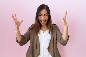 Wall Mural - Middle age chinese woman wearing glasses over pink background celebrating mad and crazy for success with arms raised and closed eyes screaming excited. winner concept