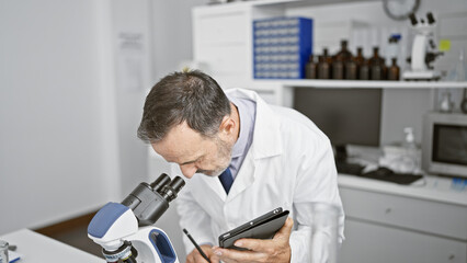 Sticker - Concentrated middle age man, a grey-haired scientist, engrossed in medical research at his lab, writing data from microscope analysis on a touchpad.