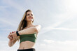 © muse studio - A strong woman uses a fitness watch for sports training. The athlete smiles portrait against the sky. Uses a smartwatch for android.