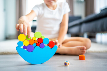 Wall Mural - Little girl playing with wooden balancing toy on the floor in home living room. Focus on balancer