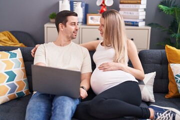 Canvas Print - Man and woman couple using laptop expecting baby at home