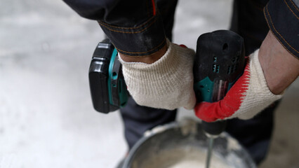 Wall Mural - The builder mixes the construction mixture in a container to direct the solution with a mixer. Mix the solution in a bucket, close-up of hands with a mixer.